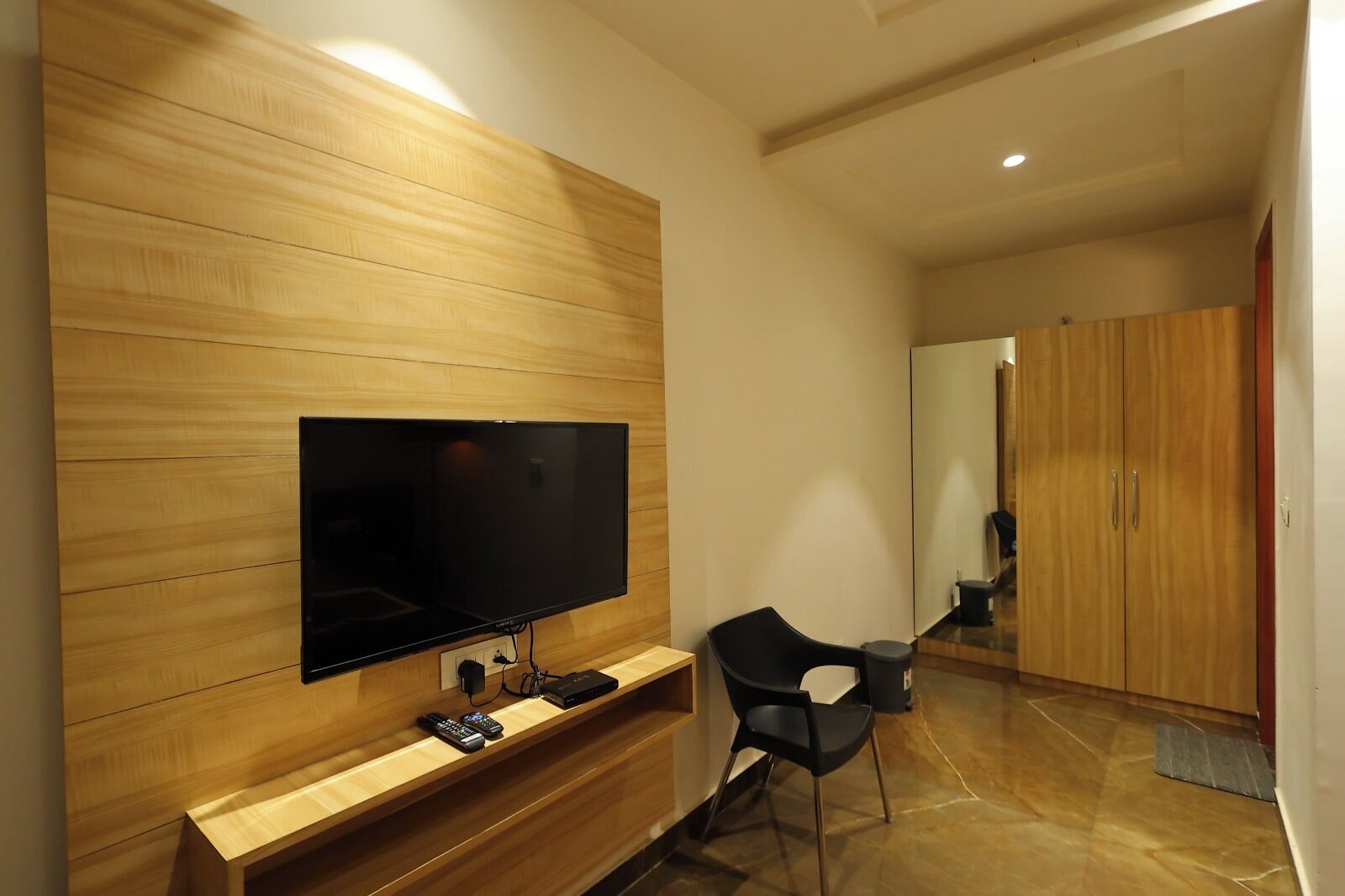 Ein modernes Wohnzimmer mit einem Flachbildfernseher an einer Holzwand, einem schwarzen Sessel und einem Holzschrank.