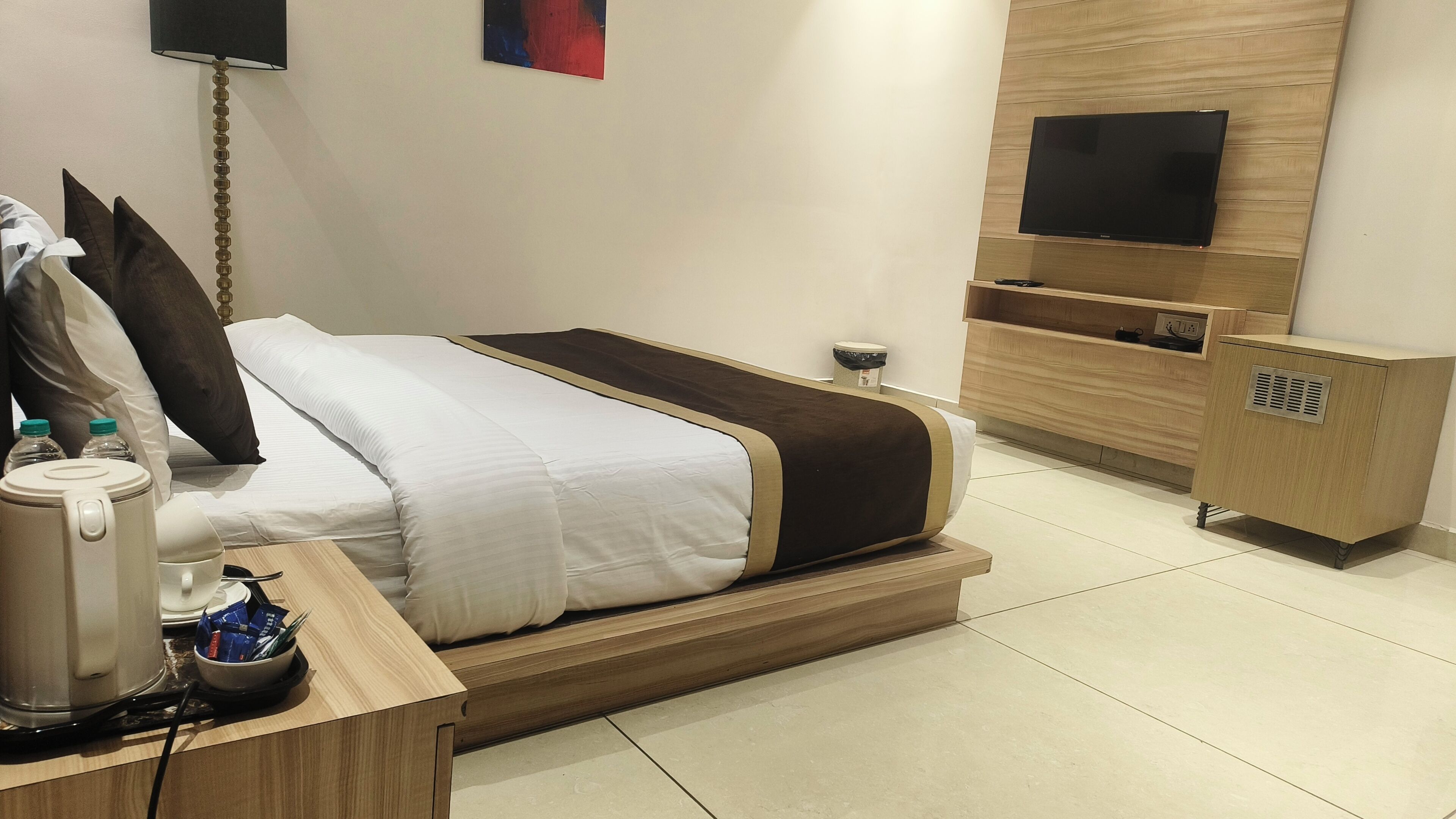 A modern hotel room with a bed, bedside table, lamp, TV, and a small cabinet.