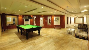 Een ruime kamer met een pooltafel, houten vloeren en een zithoek met een bank en een tafel.