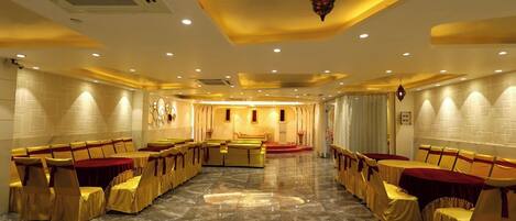 A banquet hall with rows of tables and chairs, a stage, and a decorative hanging light fixture.