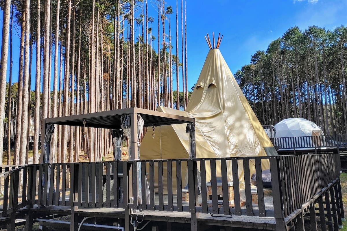 A wooden deck with a covered seating area, a tent, and a white dome structure in a forested area.