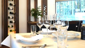Una mesa de comedor dispuesta con platos, cubiertos y copas de vino, con una bodega en el fondo.