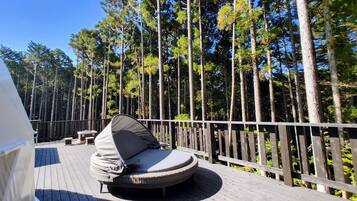 A deck with a circular seating area, surrounded by a wooden railing, overlooking a forest.