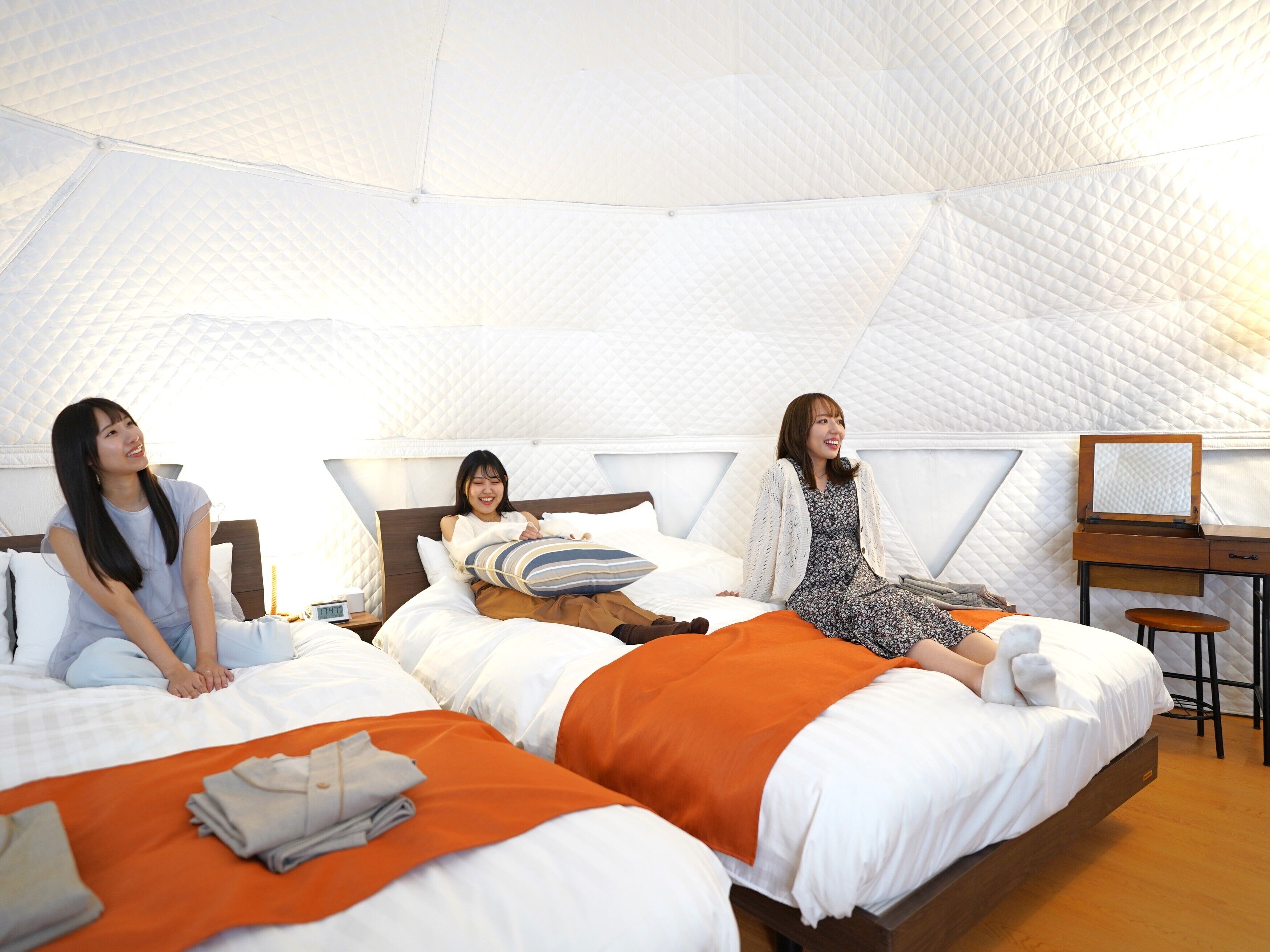 A cozy, modern tent-style room with three beds, each with a pillow and blanket.