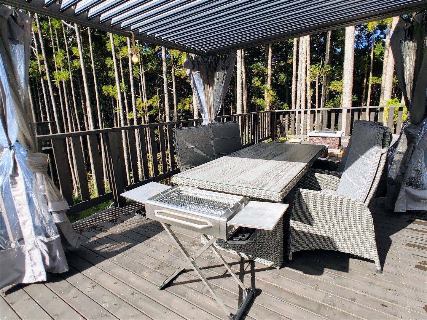 An outdoor patio with a table and chairs, surrounded by a wooden deck and a metal railing.