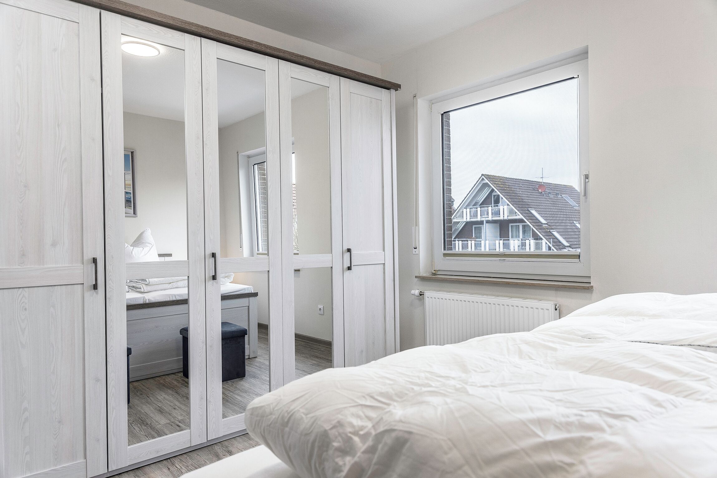 Een slaapkamer met een groot raam, een bed en een garderobe met spiegeldeuren.