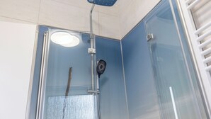 Een douche met glazen wand, een handdouche en een ventilator aan de muur.