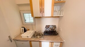 Cocina pequeña con pileta, cafetera y tostadora. Se observa una ventana sobre la pileta y un estante con vasos.