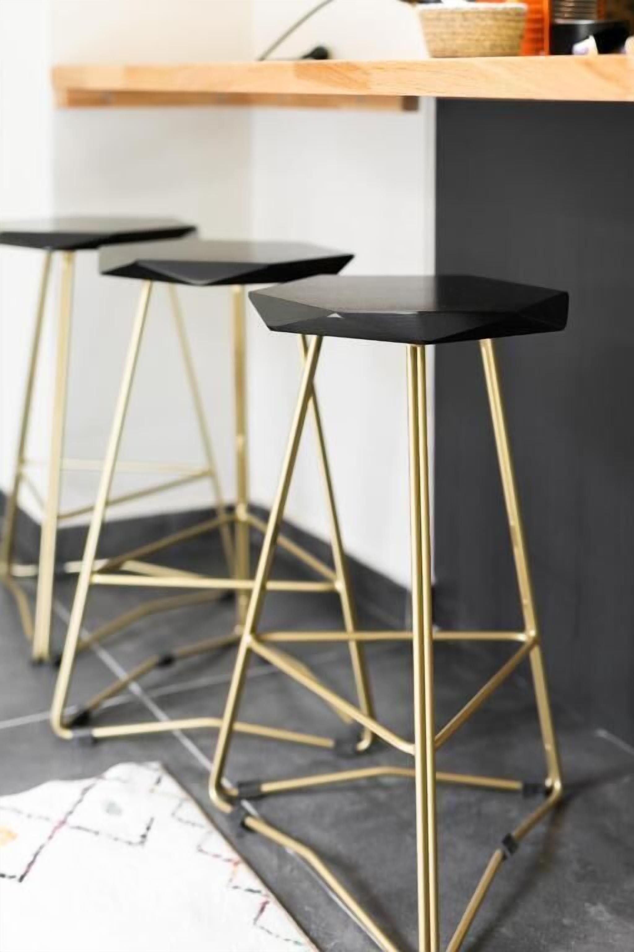 Three black bar stools with gold legs and black seats.
