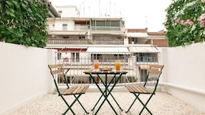 A balcony with a table and chairs, a railing, and a view of buildings in the background. - Luxury 5 by OTOTO (Thessaloniki)
