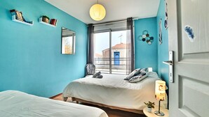 Une chambre avec deux lits, une fenêtre donnant sur un beau paysage, une lampe suspendue et une petite table avec une plante.
