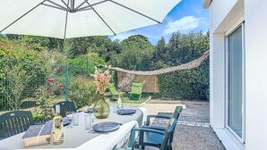 Une terrasse extérieure avec une table dressée pour le repas, entourée de chaises et d’un parasol.