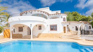 Una villa blanca con piscina, varios balcones y fachada de piedra.