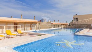 Ein Swimmingpool mit gelben Liegestühlen, einer Steinmauer und blauem Himmel.