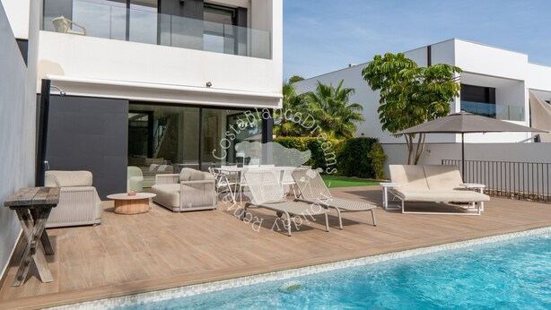 A modern outdoor pool area with lounge chairs and a table, surrounded by a wooden deck and a glass balustrade.