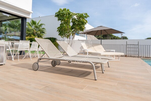 Ein Poolbereich mit Liegestühlen, einem Tisch und einem großen Sonnenschirm.