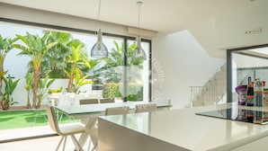 A modern kitchen with a large island, white cabinetry, and a view of a lush garden.