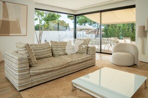 Ein modernes Wohnzimmer mit einem gestreiften Sofa, einem Glastisch und Blick auf eine Terrass'.