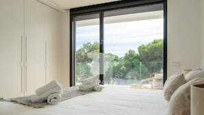 A bedroom with a bed, a large window, and a view of trees.