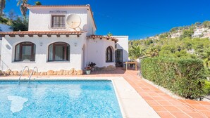 Una villa blanca con piscina, antena parabólica y vistas a la colina.