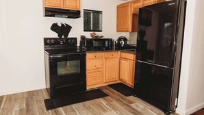 A compact kitchen with black appliances, wooden cabinets, and a black refrigerator. - Cozy Retreat Near Fort Meade | Fire Pit (Severn)