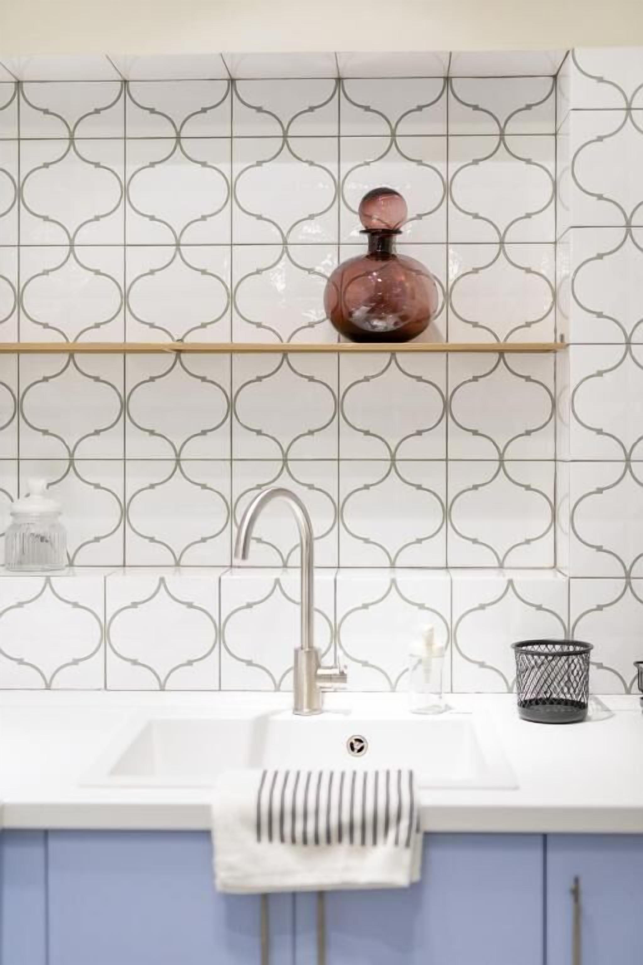 A modern kitchen with a white sink, a stainless steel faucet, and a patterned backsplash.