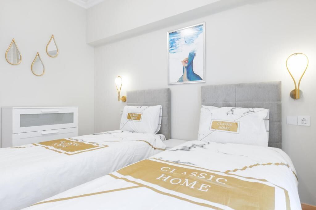 Habitación de hotel con dos camas, una mesita de noche y una lámpara fijada a la pared.