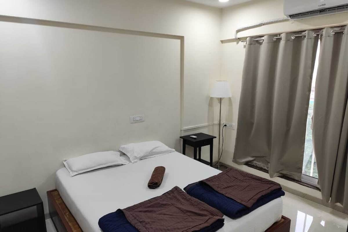 Quarto de hotel com uma cama, mesa de cabeceira, luminária e janela com cortinas.
