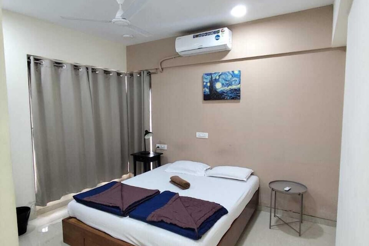 Un dormitorio con cama, mesita de noche, equipo de aire acondicionado, ventilador de techo y un cuadro en la pared.