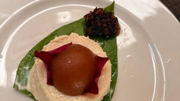 Un postre sobre un plato blanco, con una hoja verde, una esfera marrón y un adorno oscuro.
