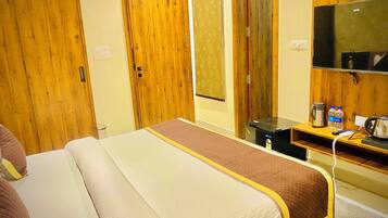 A hotel room with a bed, wooden wardrobe, a small desk with a kettle, two bottles of water, and a television.