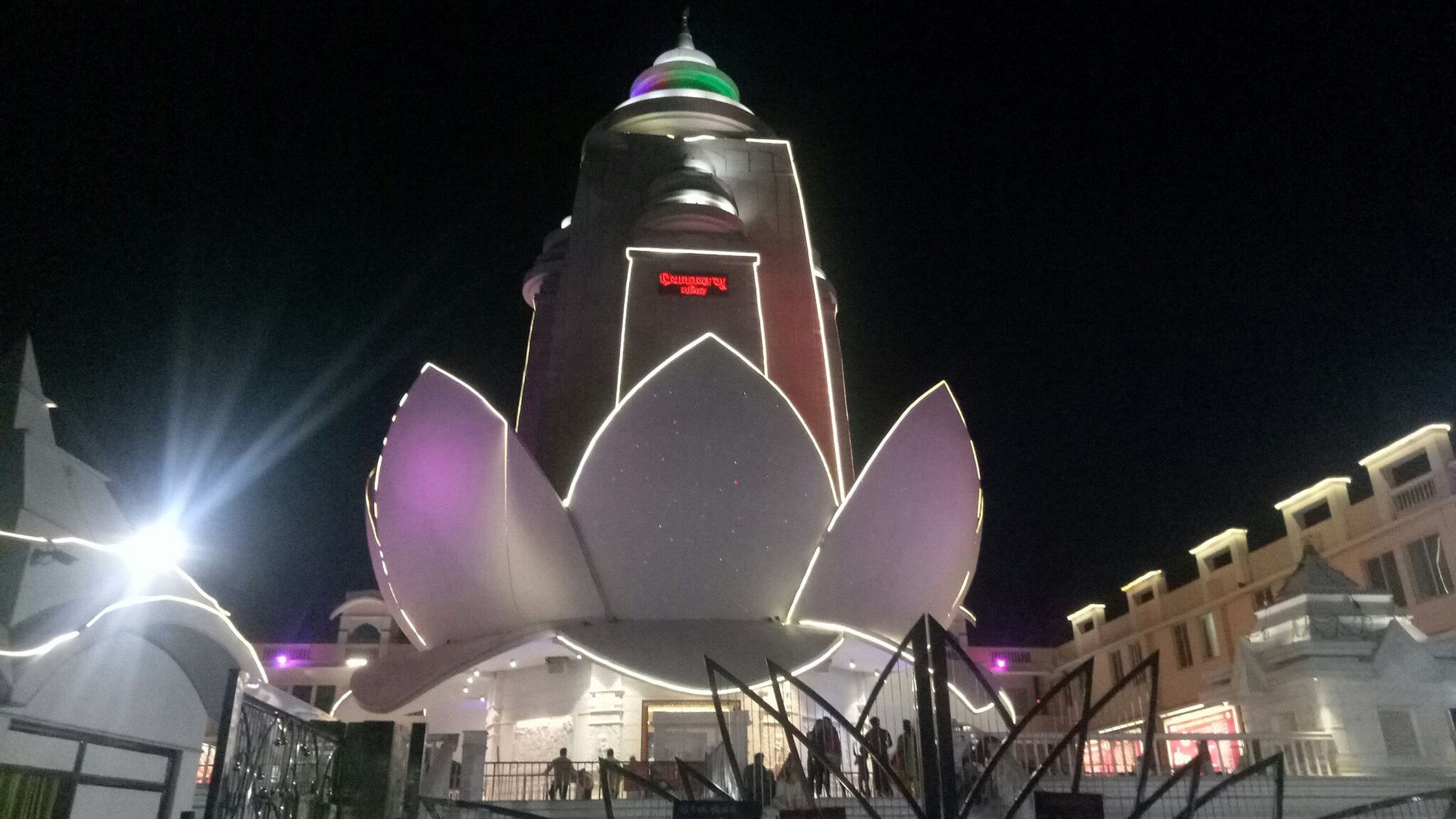 A large illuminated lotus-shaped structure in an urban setting at night.