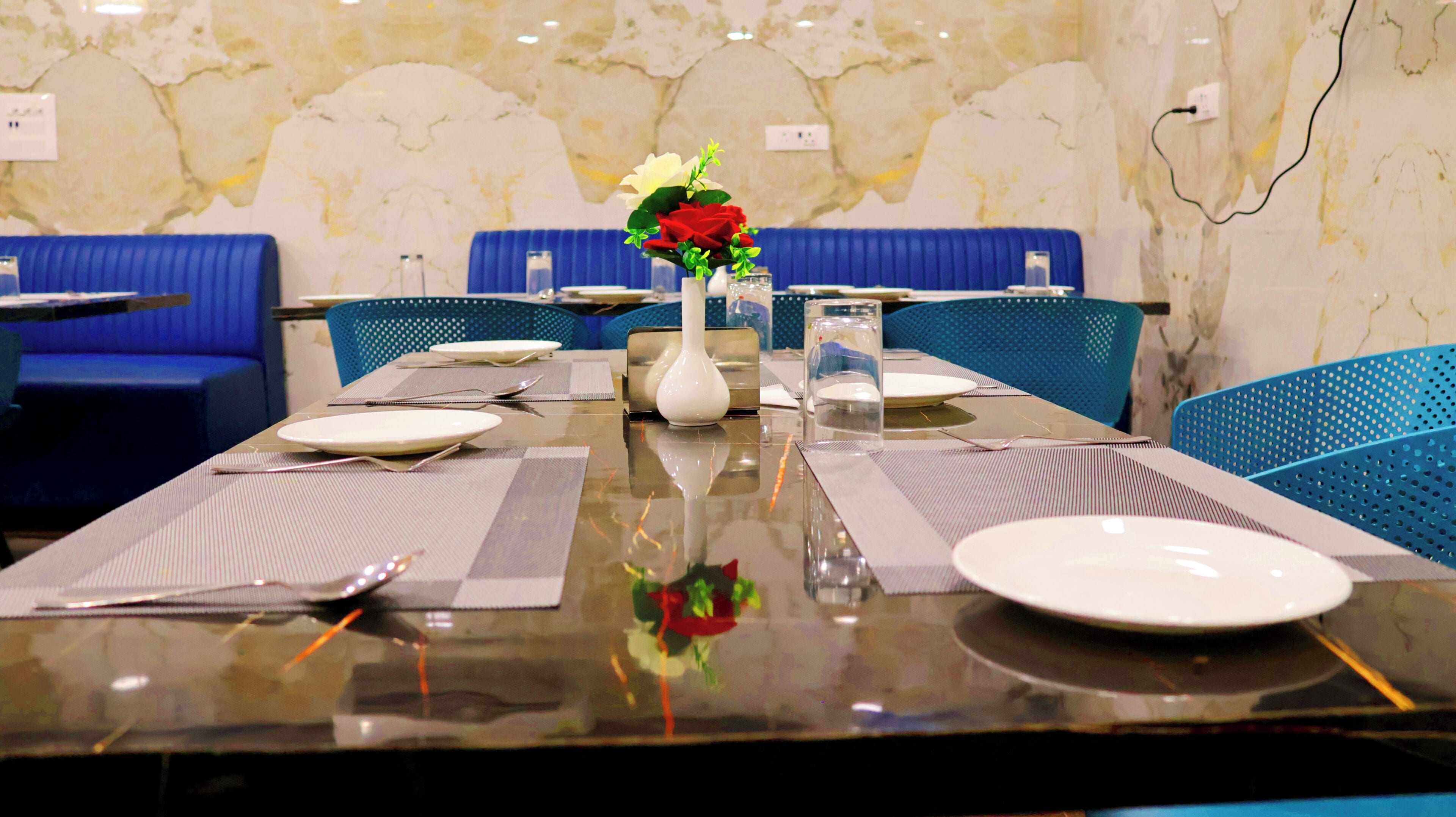 A dining table set with plates, cutlery, and a vase with flowers. Blue upholstered chairs surround the table.
