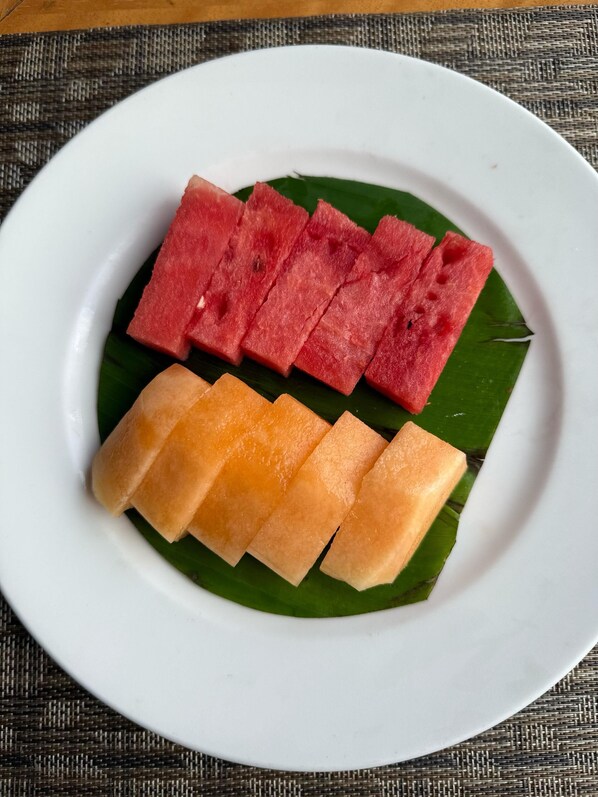 A plate with sliced watermelon and cantaloupe on a green leaf. - Hotel Tulsi Grand Inn (Vrindavan)