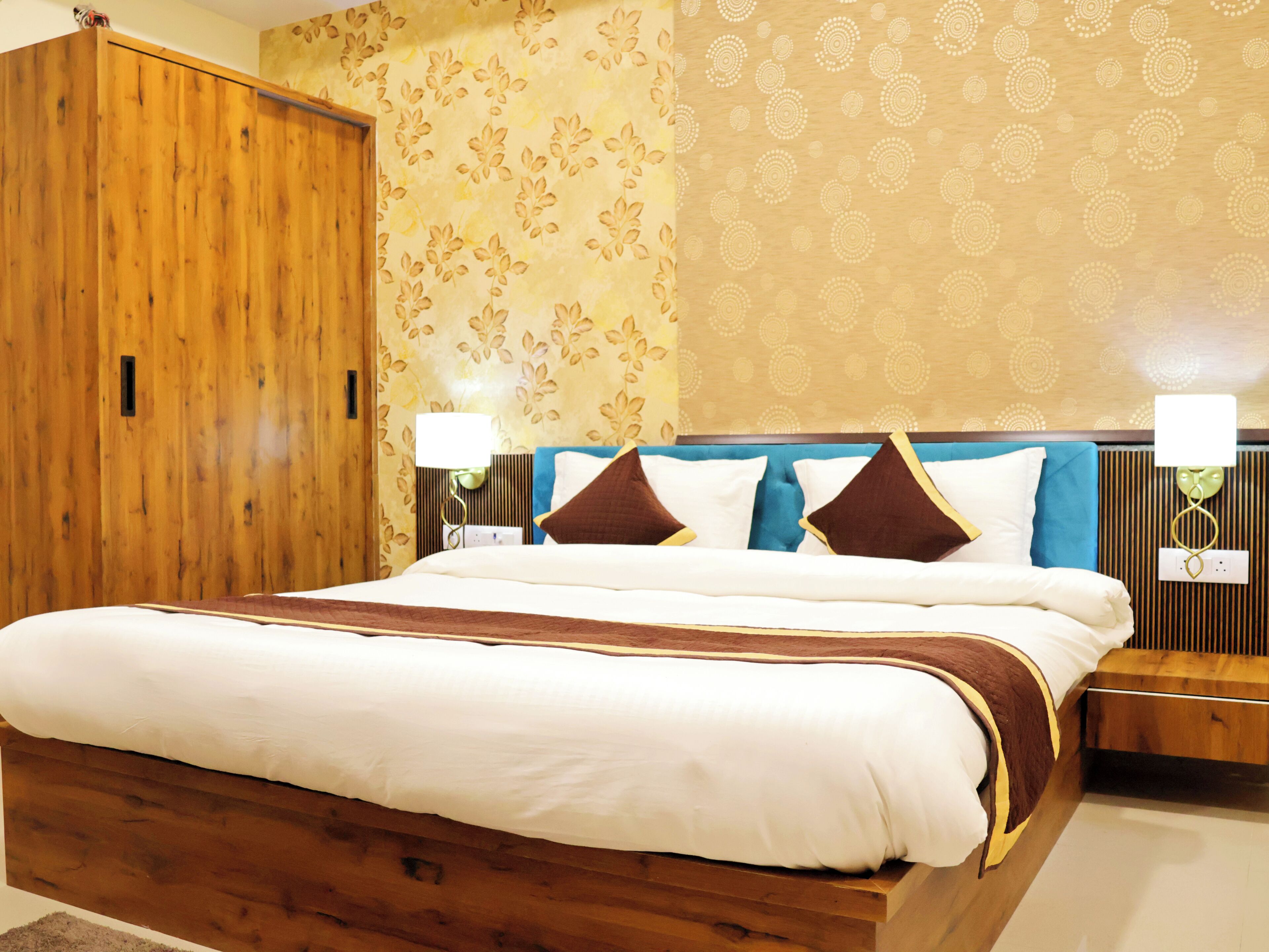 A neatly made bed with a wooden headboard, a nightstand with a lamp, and a wardrobe with a floral wallpaper pattern.