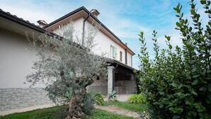 A building with a stone facade, a covered porch, and a garden with various plants. - La Casa del Lago in Manerba del Garda (Manerba del Garda)