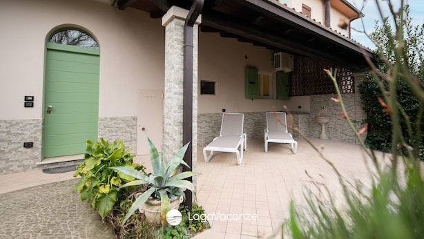 A building with a green door, two white lounge chairs, and a covered patio area with plants. - La Casa del Lago in Manerba del Garda (Manerba del Garda)