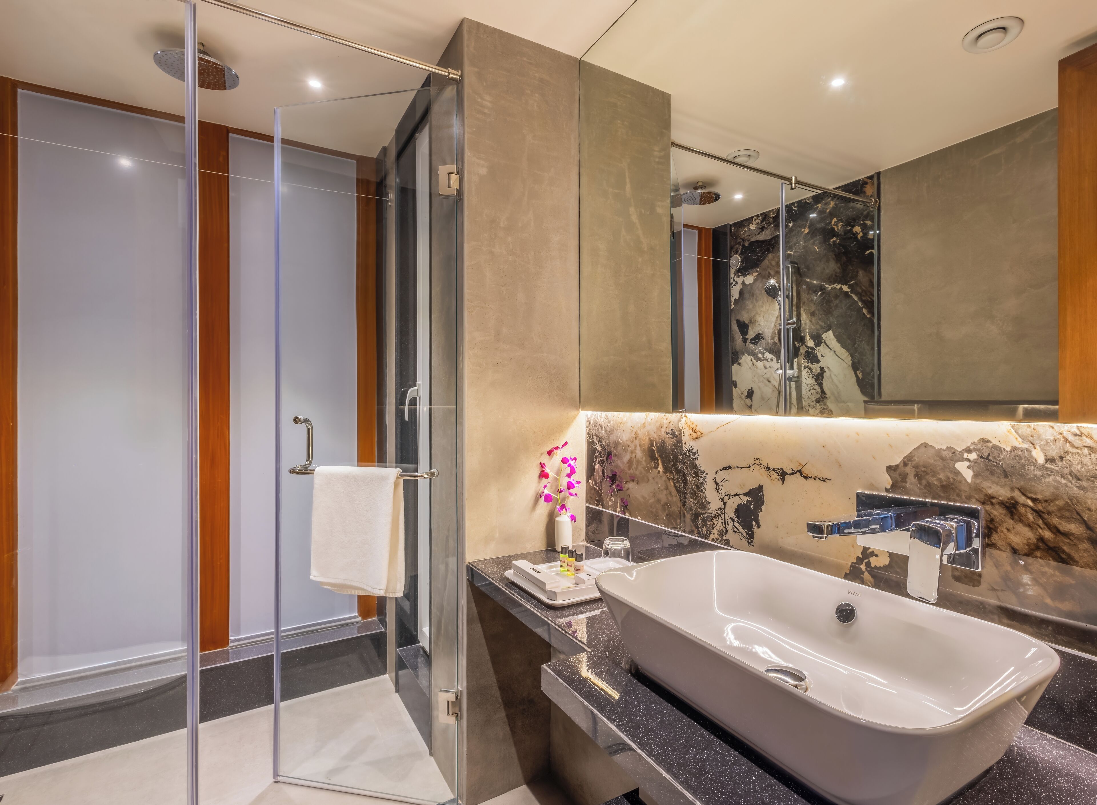 A modern bathroom with a glass-enclosed shower, a large mirror, and a marble countertop.
