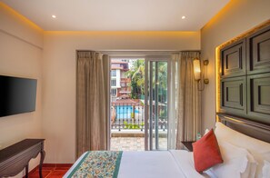 A hotel room with a bed, a TV, a desk, and a view of a pool and buildings outside. - Effotel By Sayaji Calangute, Goa (Calangute)