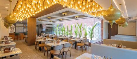 A restaurant with multiple dining areas, hanging light fixtures, and potted plants.