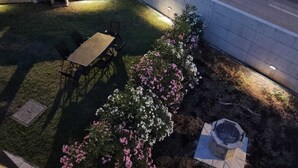 An outdoor patio area with a table and chairs, a small seating area, and a flower bed with pink and white flowers. - Apartman Sea Lake Magic 1 (Vinodol)