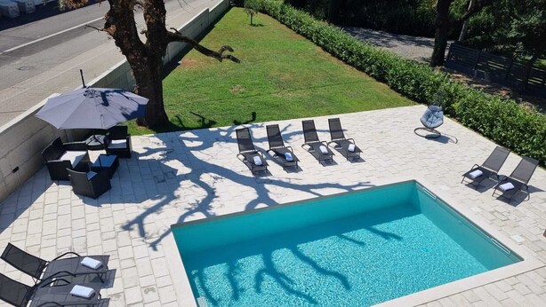 A rectangular swimming pool with a tiled deck, surrounded by lounge chairs and a small table with an umbrella. - Apartman Sea Lake Magic 1 (Vinodol)