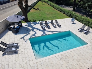 A rectangular swimming pool with a tiled deck, surrounded by lounge chairs and a small table with an umbrella. - Apartman Sea Lake Magic 1 (Vinodol)