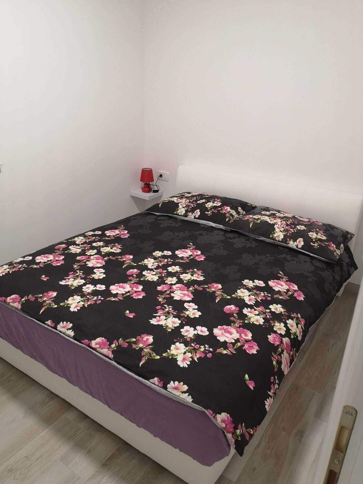 A bed with a black floral bedspread and a purple throw blanket.