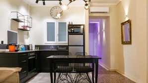 A modern kitchen with black cabinets, a dining table with wire chairs, a clock, and a pendant light.
