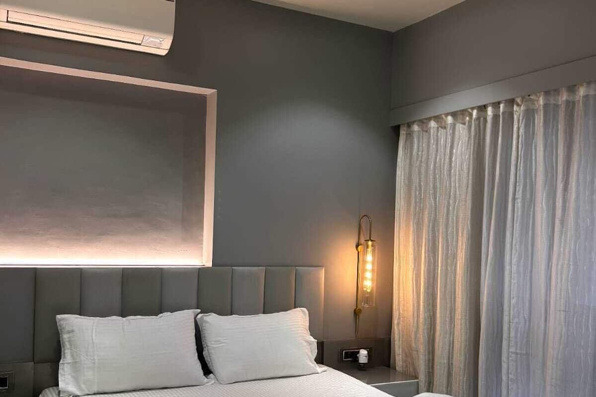 Una habitación de hotel moderna con una cama grande, un ventilador de techo, un equipo de aire acondicionado, una mesita de noche con lámpara y una ventana con cortinas.