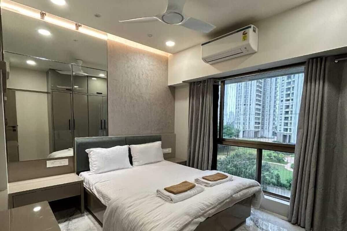 Un dormitorio moderno con una cama grande, un ventilador de techo, un equipo de aire acondicionado, un ventanal con cortinas y un armario con espejo.