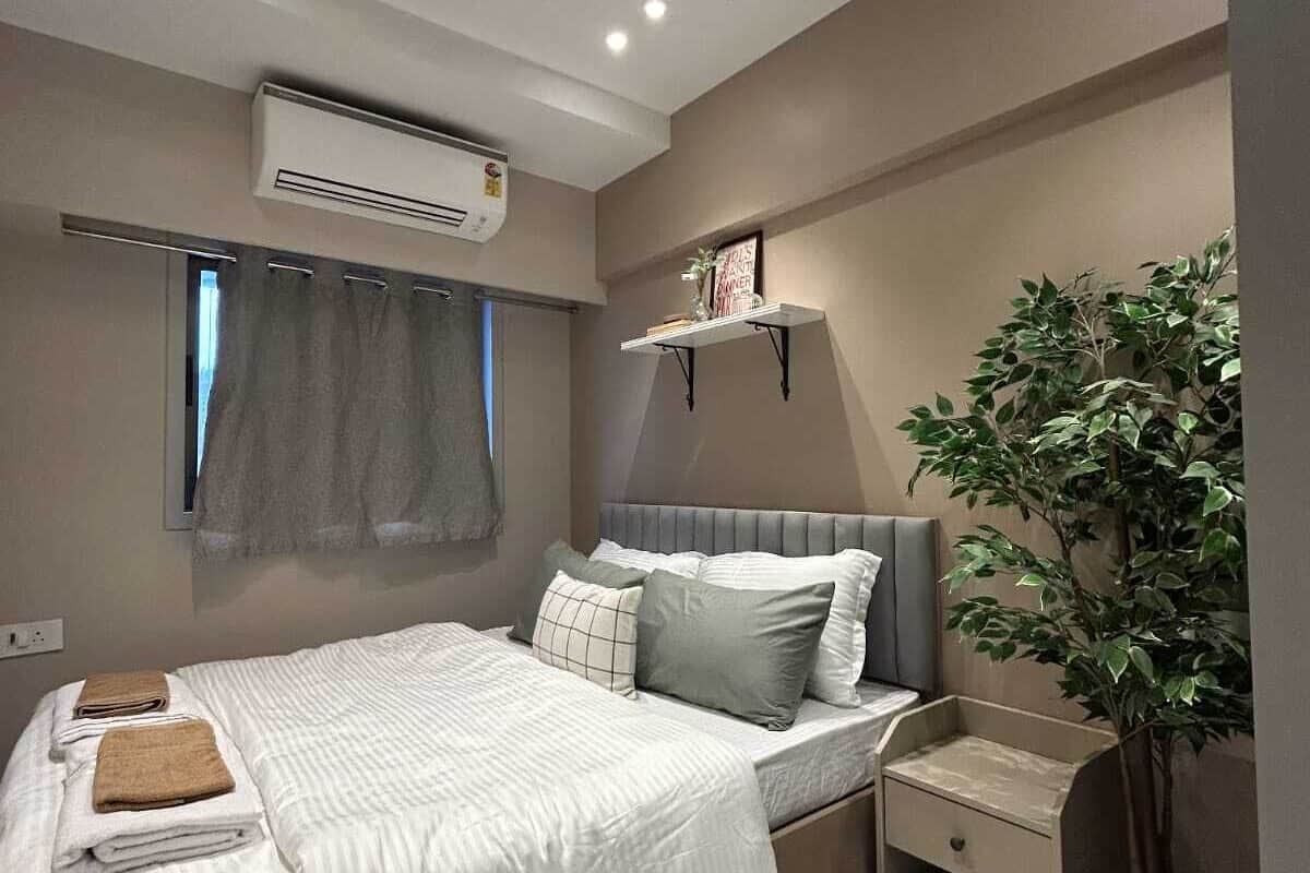 Un dormitorio moderno con cama, mesitas de noche, una planta y un equipo de aire acondicionado.