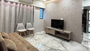 A modern living room with a sofa, two chairs, a TV, and a ceiling fan. - Southside by Daily Stays (Mumbai)