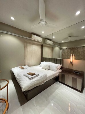 A modern bedroom with a bed, bedside tables, a mirror, and a ceiling fan. - Southside by Daily Stays (Mumbai)